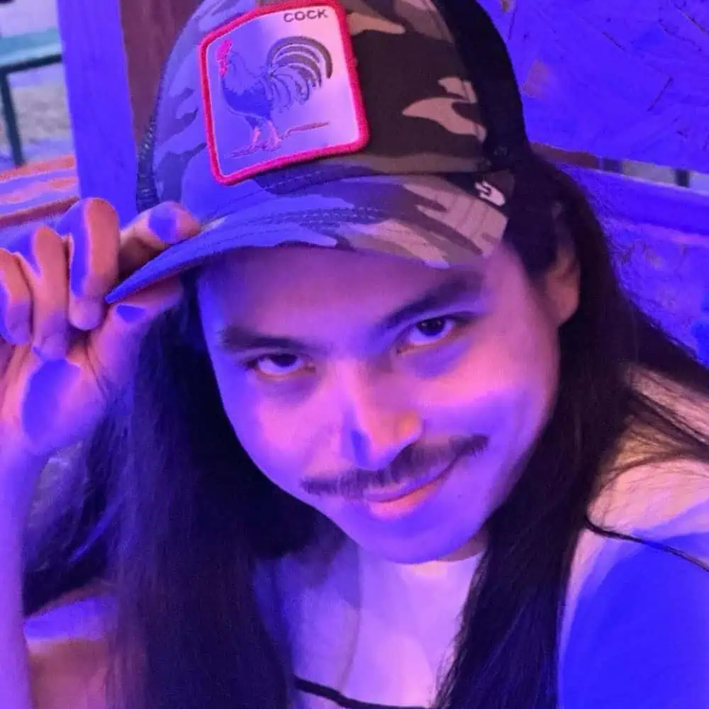 Alex Zee cheekily tipping his cap in bisexual lighting.