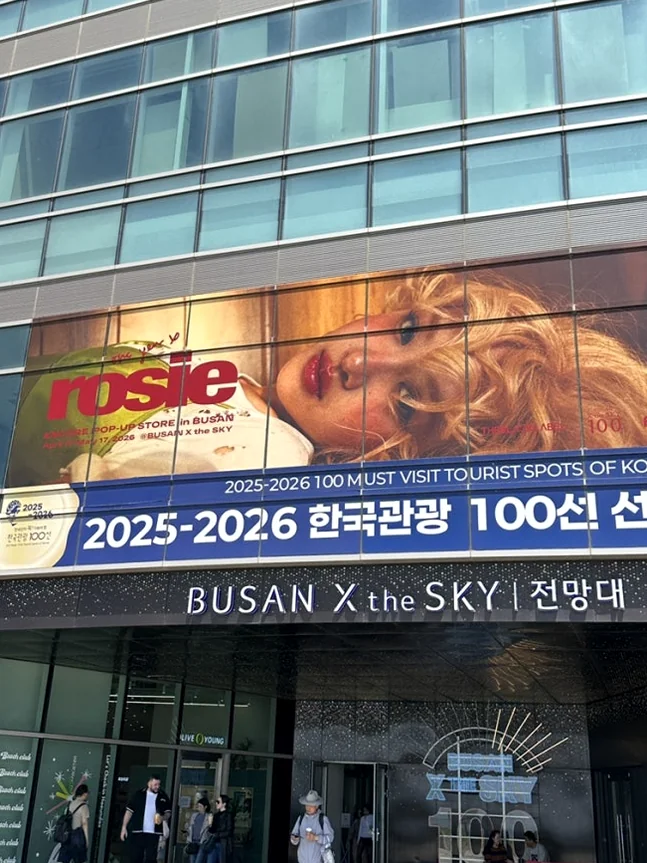 A striking panoramic view of the BUSAN X the SKY building, adorned with a large, eye-catching pop-up store banner that signifies the event's arrival in Busan - ROSÉ ENCORE POP-UP in BUSAN: A Deep Dive into 'one year of rosie' at BUSAN X the SKY