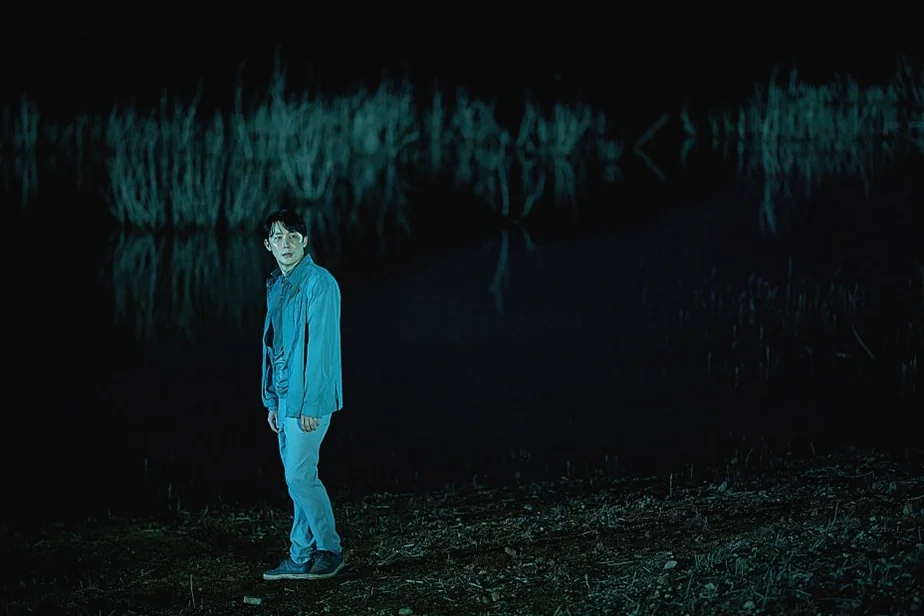 高い葦に囲まれた神秘で暗い湖のほとりに立つ男性の広角ショット - 韓国を震撼させる映画『サルモクチ』の世界。忠清南道・礼山への聖地巡礼ガイド