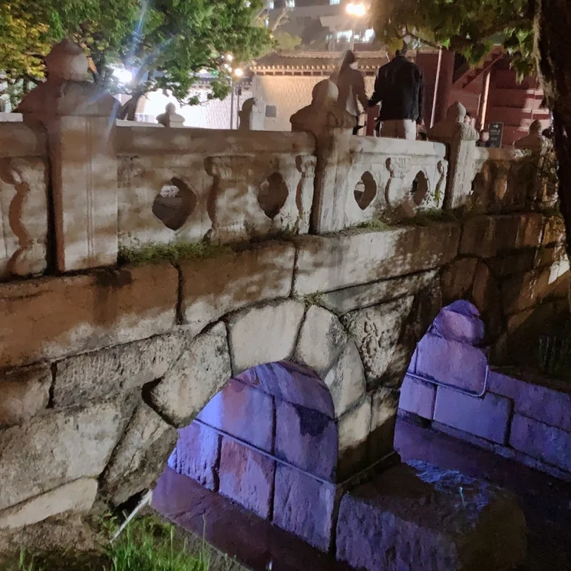 モダンな紫色の照明でハイライトされた、古代の石橋のアーチのクローズアップ - 2026年ソウル、夜の王宮を彩る光の祭典。昌慶宮'水光蓮花'完全ガイド