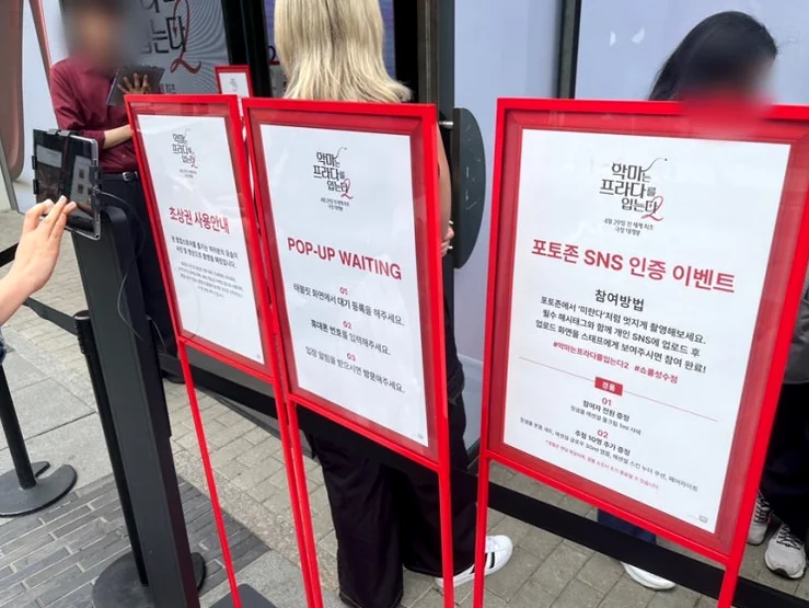 A lively scene at the pop-up store entrance, showing the queue and various information boards, capturing the vibrant atmosphere with actual visitors. - The Devil Wears Prada 2: An Exclusive Pop-Up Showroom Experience in Seoul's Seongsu District