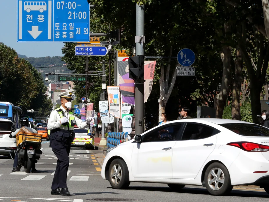 A striking vertical top-down view of a dark sedan yielding to pedestrians at a geometric zebra crossing - Navigating the Pause: The Essential 2026 Guide to Korea’s Right-Turn Regulations