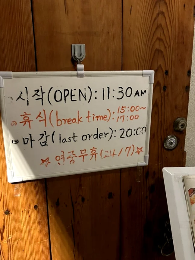 A handwritten sign on the wooden door displaying the daily operating and break hours - A Sanctuary of Plant-Based Heritage: Exploring the 100-Year-Old Hanok of Vegan Insa