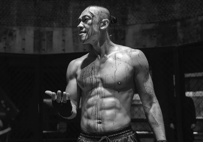 戦闘準備を整え、汗と汚れにまみれた筋肉質なファイターがケージの中に立つドラマチックな白黒カット - 2026年注目作『ブラッドハウンド』シーズン2：圧倒的肉体美とノワールアクションの深淵へ