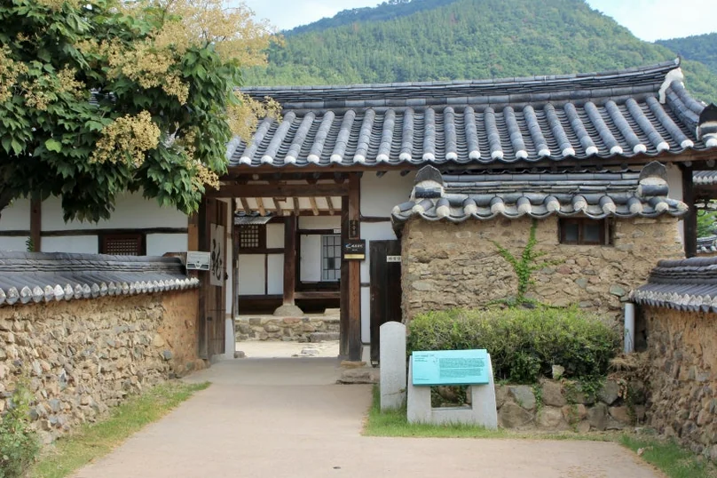 The dignified entrance of a traditional Hanok house, framed by lush green trees and ancient stone walls under a clear sky. - A Sanctuary of Scholarly Grace: Exploring the Timeless Otgol Village in Daegu