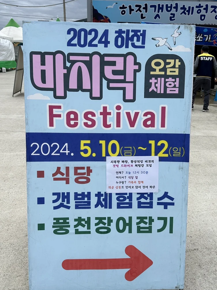 alt: デジタルオーバーレイのない、自然光と現実世界の質感でフェスティバルのスケジュールと方向を示す、現場の物理的な案内板。 - 『K-Life Hack』厳選！高敞ハジョンアサリ五感体験フェスティバルで贅沢な韓国の自然を満喫する旅