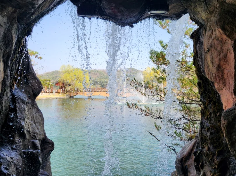 滝の裏側から眺める幻想的な視点。落ちる水越しに周囲の自然を芸術的に捉えたショット。 - 癒やしと歴史が交差する、忠清北道・堤川「義林池」の極上トラベルガイド