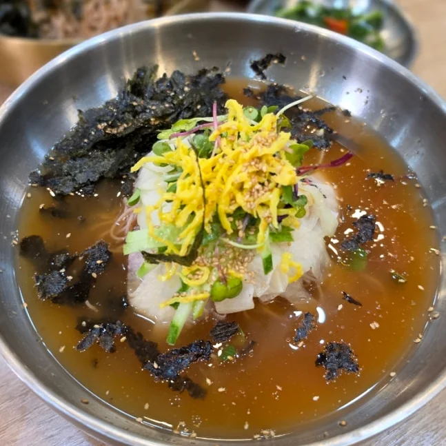 色彩豊かで食欲をそそる冷やしメミル麺のクローズアップ。地元の美食の質感を伝えます。 - 癒やしと歴史が交差する、忠清北道・堤川「義林池」の極上トラベルガイド