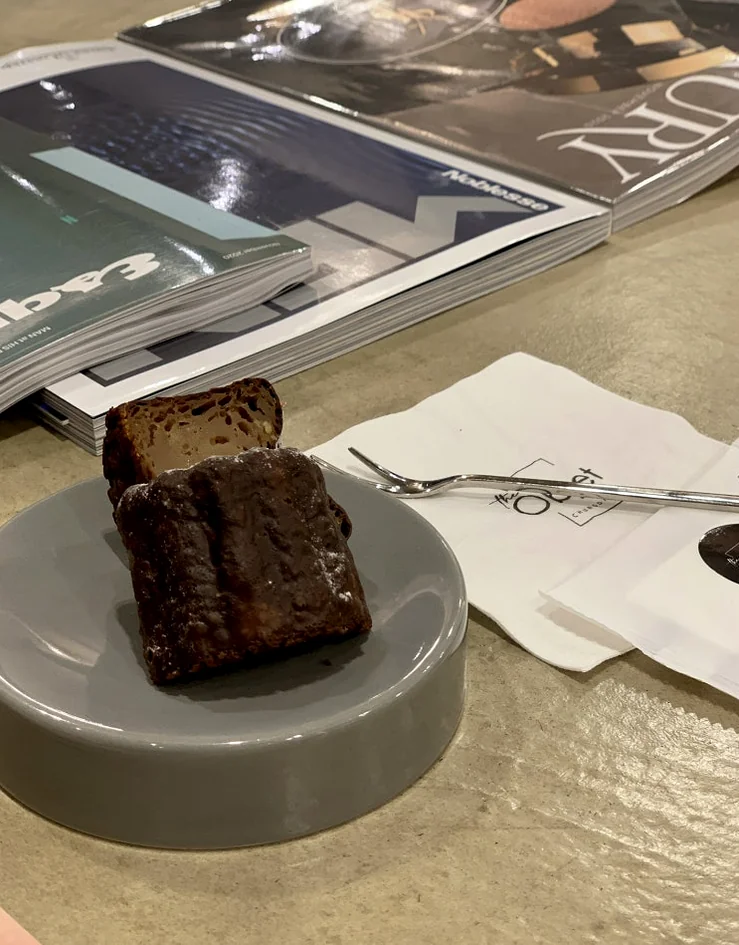 Lifestyle detail of a canele dessert served on a minimalist plate beside high-end lifestyle magazines - Architectural Volume: The Discerning Expats Guide to The Objet Cheongdam