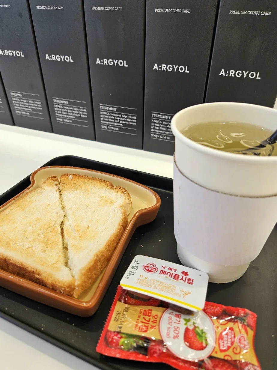 Complimentary snack service featuring toast and a beverage with branded product packaging in the background - Beyond the Neon: The Precision of K-Beauty Mastery at Argyol Hongdae