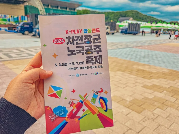 alt="安東の祝祭会場を背景に、公式ガイドブックを手にして旅を楽しむ観光客の姿" - 2026年5月の韓国旅行、安東（アンドン）へ。伝統と遊びが融合する「車戦将軍・魯国公主祭り」完全ガイド