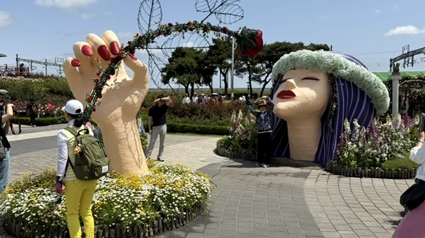 Whimsical floral sculptures of a giant hand and face create a surreal and artistic atmosphere within the park's expansive rose garden. - The Floral Monarchy: Rediscovering Nostalgia at Gokseong Seomjingang Train Village