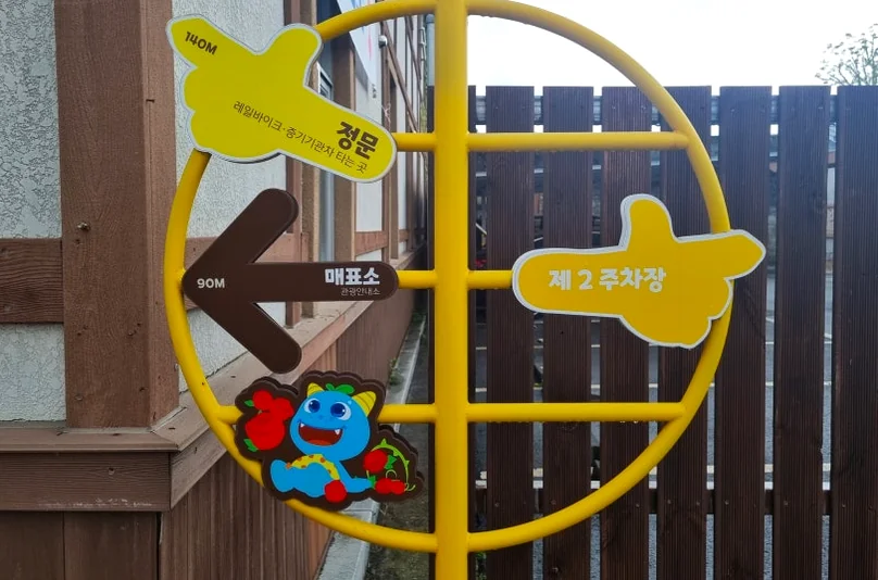 Yellow directional signage providing navigation for visitors; a functional element of the park's physical environment. - The Floral Monarchy: Rediscovering Nostalgia at Gokseong Seomjingang Train Village