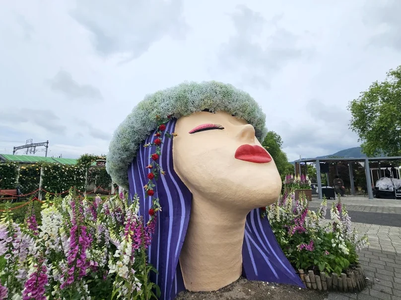 A detailed close-up of the giant face sculpture, emphasizing the texture of the moss and the vividness of the floral 'hair'. - The Floral Monarchy: Rediscovering Nostalgia at Gokseong Seomjingang Train Village