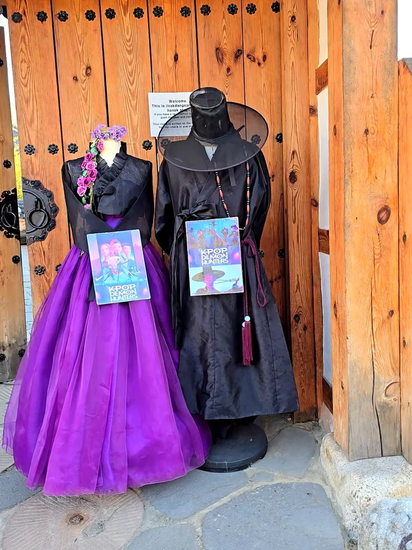 伝統的な韓屋の木製門にマネキンが着用した黒と紫の韓服が飾られています。 - 全州韓屋村で優雅な韓服体験：『貴族衣装室』で叶える特別な一日