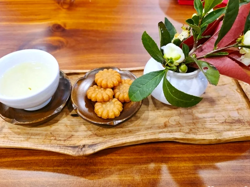 alt="伝統的な韓国茶、薬菓（ヤックァ）、繊細な椿の花のアレンジメントが並ぶ、プレミアムなお茶文化を紹介する美しい木製トレイ" - 智異山の静寂を味わう：河東（ハドン）野生茶博物館で体験する韓国最高級のお茶文化ガイド