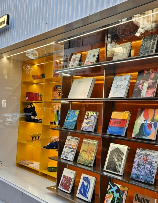 A captivating street-facing window display of MoMA Bookstore Seoul, featuring an artful arrangement of colorful books and design objects on vibrant yellow shelves, drawing in passersby with its visual appeal.</div - MoMA Bookstore Seoul: A Curated Sanctuary for Art and Design