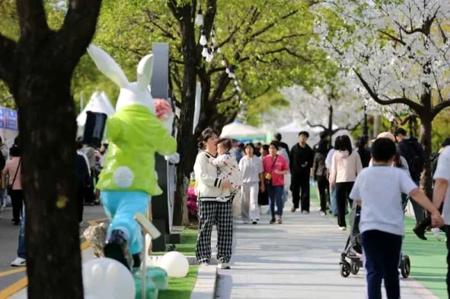 A young couple and families walking down a blossom-lined path decorated with a whimsical rabbit mascot, capturing the joyful essence of spring travel. - Verdant Sophistication at Yanggu Leports Park: The 2026 Youth Gomchwi Festival Guide