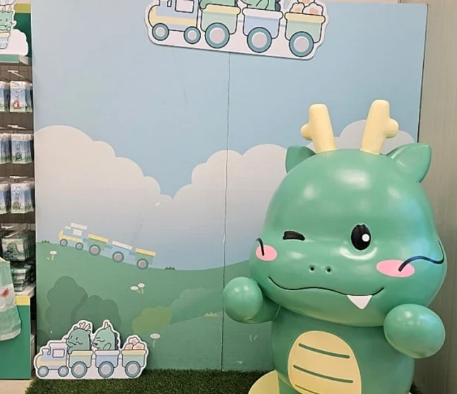 A large, winking Joayong character statue, a key highlight of the pop-up store, stands proudly amidst a charming backdrop of rolling hills and train tracks, evoking a whimsical journey. - Joayong's Popcorn Journey: E-Mart Borajum's Premier Character Pop-Up