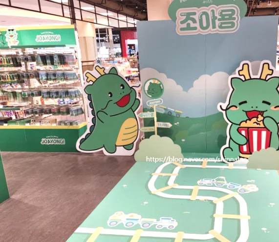The playful ambiance of the Joayong pop-up store is captured, with cheerful character cutouts enjoying popcorn and a charming train track design on the floor, enhancing the immersive experience. - Joayong's Popcorn Journey: E-Mart Borajum's Premier Character Pop-Up