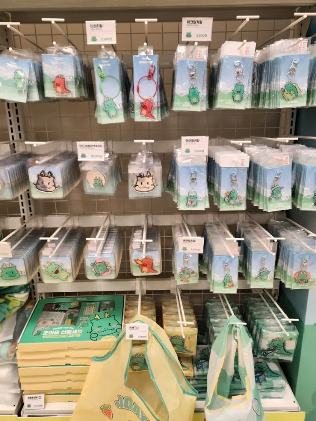 Shelves neatly organized with Joayong-themed lifestyle goods, including stylish tote bags and smaller packaged items, perfect for everyday use or as delightful souvenirs. - Joayong's Popcorn Journey: E-Mart Borajum's Premier Character Pop-Up
