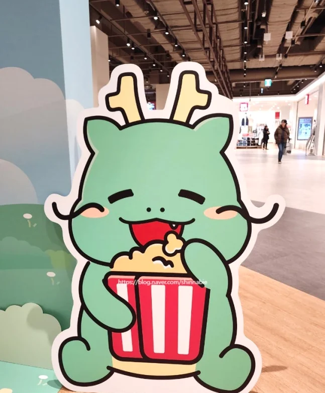 A delightful cardboard cutout of Joayong joyfully savoring popcorn, adding a touch of playful charm and photo-op potential to the pop-up store's vibrant decor. - Joayong's Popcorn Journey: E-Mart Borajum's Premier Character Pop-Up