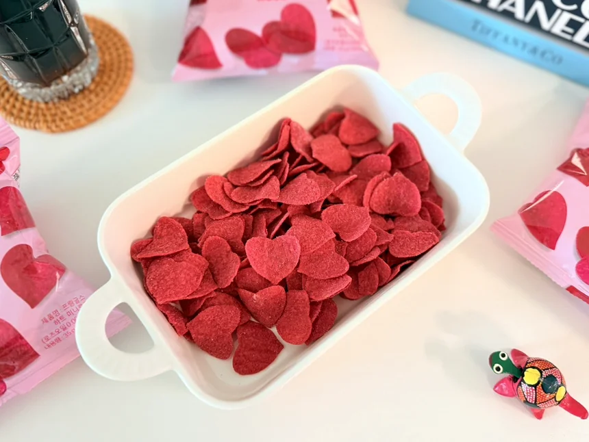 鮮やかな赤いハート型のプリングルズ・チップスがたっぷりと入った清潔感のある白いボウルの接写。独特の形状と魅力的な色彩が視覚的な楽しさを提供する。 - 韓国限定・世界初の上陸。メガボックスとGSザ・フレッシュで出会う「プリングルズ・ハート・ミニ・ローズ」の誘惑