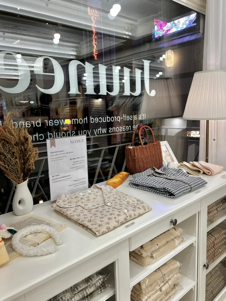 A sleek white A-frame sign positioned at the entrance, clearly guiding visitors to the 'Pajamas Boutique' on the 2nd floor, subtly enhancing the brand's visibility and accessibility. - Beyond Comfort: The Curated Pajama Sanctuary of Yeonnam-dong, Juuneedu Showroom