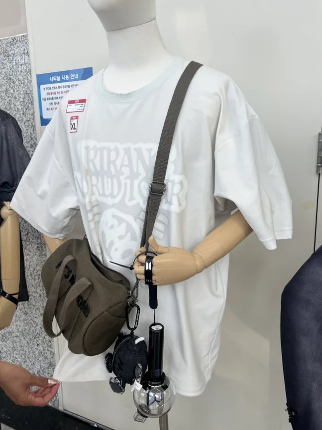 A mannequin setup showcasing the white tour t-shirt paired with a shoulder bag and light stick - BTS Arirang World Tour: A Masterpiece of Cultural Heritage and Global Modernity