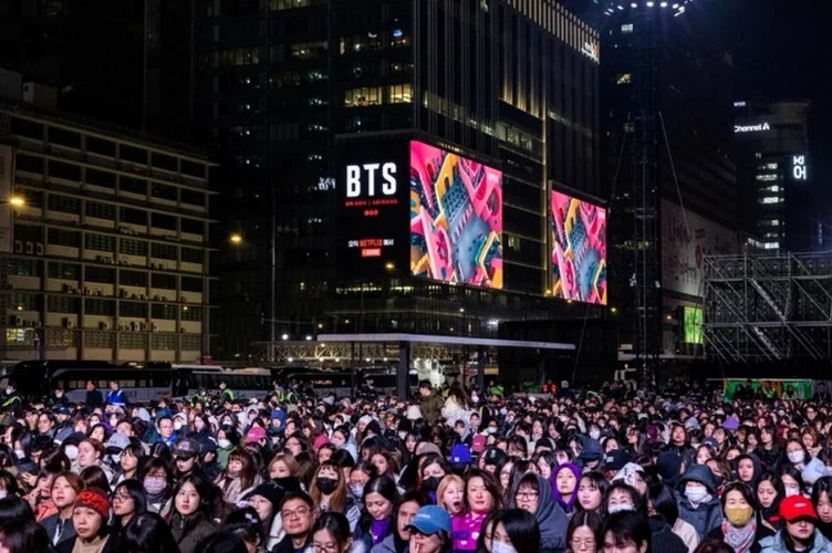 The city night view featuring a massive digital billboard showing BTS to a large crowd - BTS Arirang World Tour: A Masterpiece of Cultural Heritage and Global Modernity