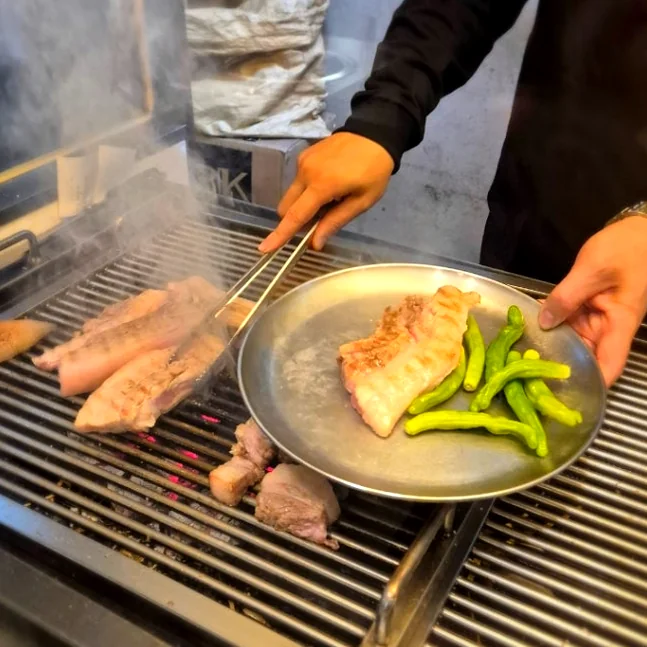 Pork belly being grilled with green peppers on a metal grate - 済州島・西帰浦で見つけた、至高の黒豚体験。麦わらの香りを纏う「Hwago(ファゴ)」の誘惑
