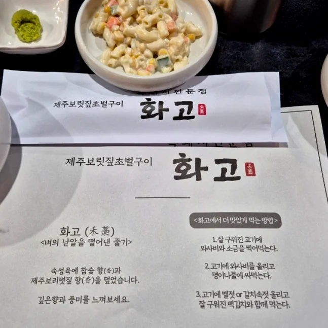 Paper table mat with Hwago logo and a bowl of macaroni salad - 済州島・西帰浦で見つけた、至高の黒豚体験。麦わらの香りを纏う「Hwago(ファゴ)」の誘惑