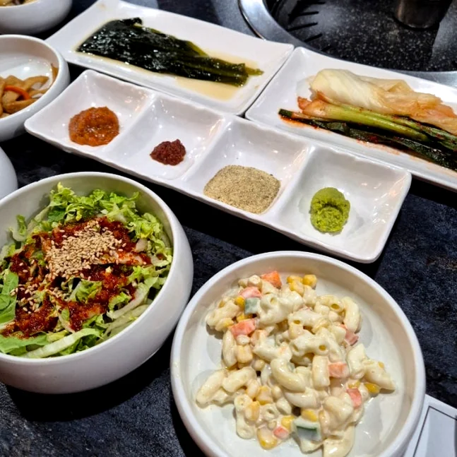 Various side dishes including green onion kimchi, lettuce salad, and dipping sauces - 済州島・西帰浦で見つけた、至高の黒豚体験。麦わらの香りを纏う「Hwago(ファゴ)」の誘惑
