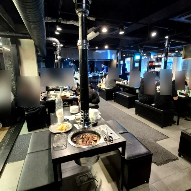 Indoor dining area with black tables and overhead exhaust pipes - 済州島・西帰浦で見つけた、至高の黒豚体験。麦わらの香りを纏う「Hwago(ファゴ)」の誘惑