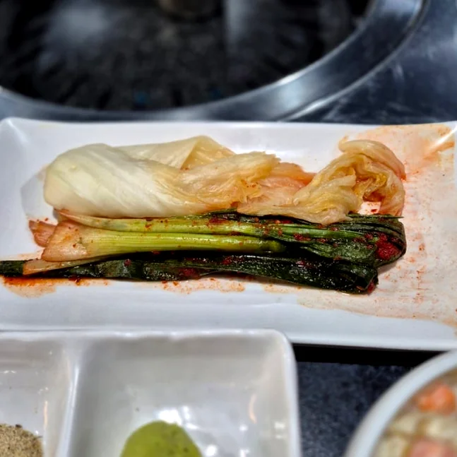 Plate of white cabbage kimchi and green onion kimchi - 済州島・西帰浦で見つけた、至高の黒豚体験。麦わらの香りを纏う「Hwago(ファゴ)」の誘惑