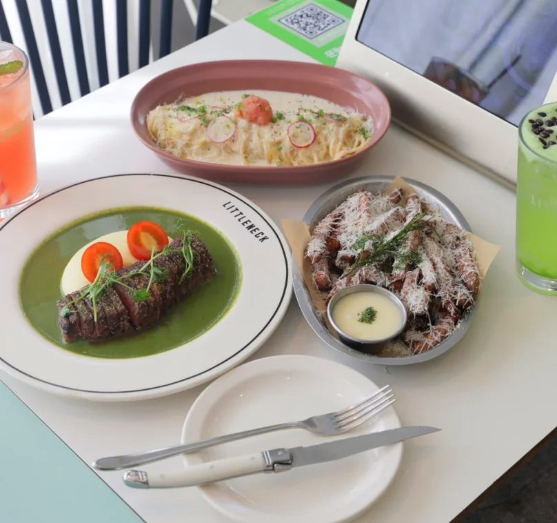 A white table set with a steak, cream pasta, a salad, and two drinks, with 'LITTLENECK' logo on a plate. - 漢南洞のアイコン 'LITTLENECK' 完全攻略。プレミアムな週末ブランチと最新ショールーム巡り ✨