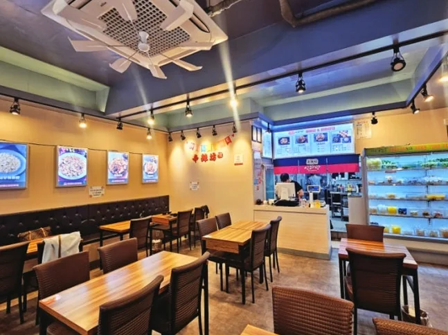 Interior dining area with wooden tables, black chairs, and ingredient display fridge - ソウル・新堂洞の路地裏で見つけた、心まで満たされるシビ辛の聖地：新羅坊（シルラバン）マラタン