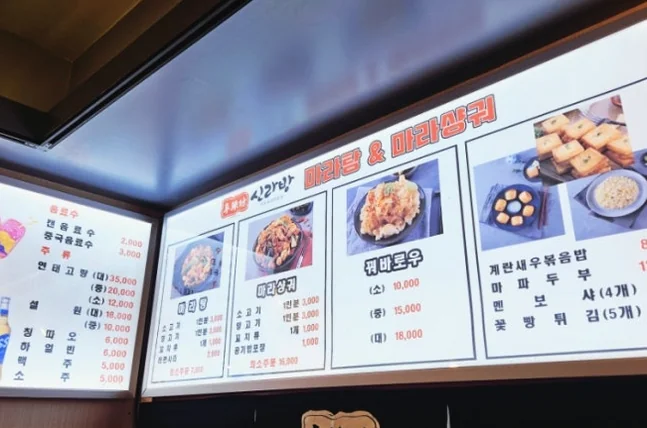 Backlit menu boards showing photos of Maratang and Guo Bao Rou with price lists - ソウル・新堂洞の路地裏で見つけた、心まで満たされるシビ辛の聖地：新羅坊（シルラバン）マラタン
