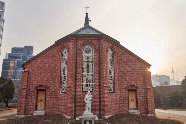 Side exterior view of Yakhyun Catholic Church, featuring red brick walls, multiple arched windows, and a side view of its spire. - ソウル駅の裏側に眠る130年の物語。中林洞・薬峴聖堂(ヤッキョンソンダン)で巡る歴史と美学の散歩道