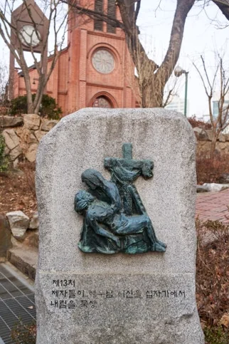 Angled view of Yakhyun Catholic Church's full exterior, highlighting its red brick architecture, tall spire, and surrounding winter landscape. - ソウル駅の裏側に眠る130年の物語。中林洞・薬峴聖堂(ヤッキョンソンダン)で巡る歴史と美学の散歩道