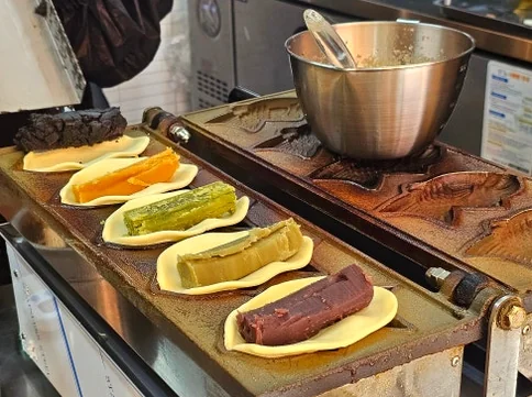 Mochi Taiyaki shells filled with colorful pastes (red bean, matcha, orange, purple sweet potato) on a cooking plate. - A Masterclass in Gluten-Free Snacking: Mochi Taiyaki at Mojjibangatgan Yeonnam