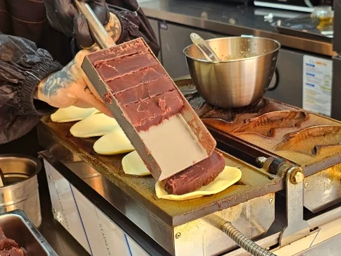 Person adding red bean paste onto mochi dough placed in a fish-shaped mold on a cooking machine. - A Masterclass in Gluten-Free Snacking: Mochi Taiyaki at Mojjibangatgan Yeonnam