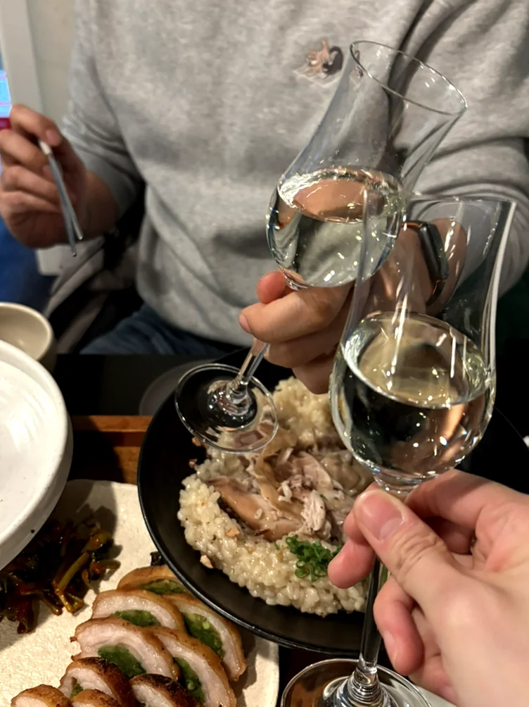 Two hands toasting with glasses of clear alcohol over a table of food - 2026年ソウル・新堂洞の最旬スポット。伝統酒ソムリエが贈る至福の韓食ダイニング『ピョジュ(表酒)』へ。