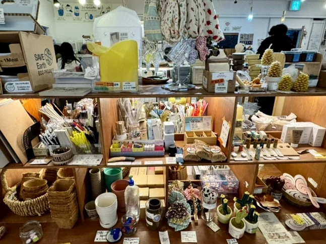 Wooden display shelves filled with various zero-waste lifestyle products in an indoor setting - 2026年最新｜ソウル・望遠洞(マンウォンドン)のエコ＆感性散策。ゼロウェイストの聖地'アルメン商店'と南仏カフェ'リトルメドウ'
