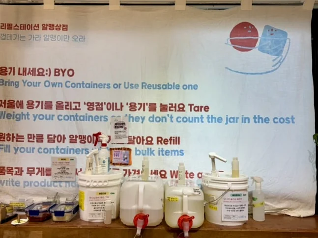 Refill guide banner with text and illustrations hanging over liquid detergent dispensers - 2026年最新｜ソウル・望遠洞(マンウォンドン)のエコ＆感性散策。ゼロウェイストの聖地'アルメン商店'と南仏カフェ'リトルメドウ'