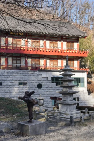 A large multi-story traditional building with a stone pagoda and a bronze martial arts statue - 慶州「骨窟寺（コルグルサ）」：1500年の時を刻む石窟寺院と、身心を整える「禅武道」の聖地へ