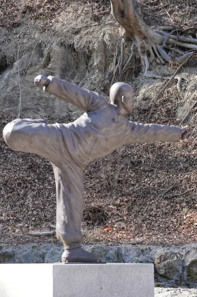 A close-up of a bronze statue performing a Sunmudo martial arts pose against a wooded background - 慶州「骨窟寺（コルグルサ）」：1500年の時を刻む石窟寺院と、身心を整える「禅武道」の聖地へ