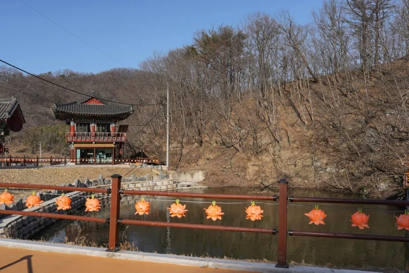 A row of orange lotus lanterns attached to a wooden fence next to a pond - 慶州「骨窟寺（コルグルサ）」：1500年の時を刻む石窟寺院と、身心を整える「禅武道」の聖地へ