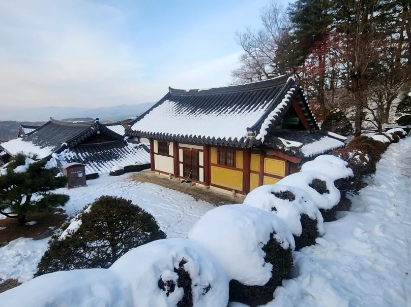 Stone pagoda in a snow-covered temple courtyard with a main building in the background. - 時を止めた千年古刹、安東・鳳停寺(ポンジョンサ)へ。韓国最古の木造建築と出会う静謐な旅