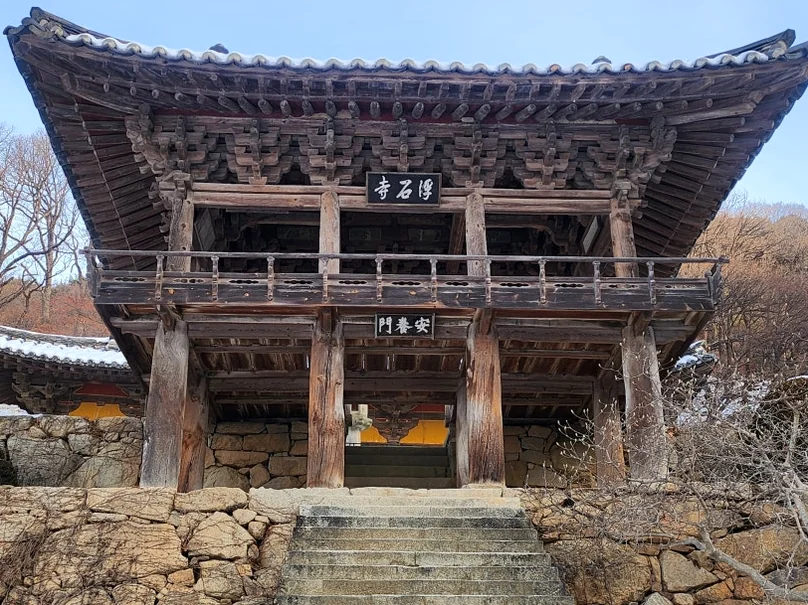 Stone pathway winding through snow-covered temple grounds with traditional buildings and sunset light. - 時を止めた千年古刹、安東・鳳停寺(ポンジョンサ)へ。韓国最古の木造建築と出会う静謐な旅